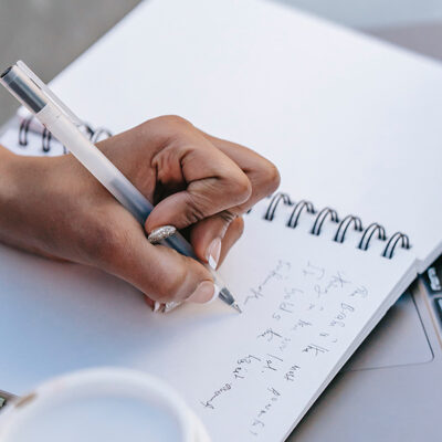 A person writing in a notebook with a pen.